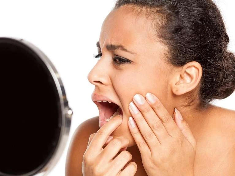 A woman looks worried as she sees her teeth in mirror