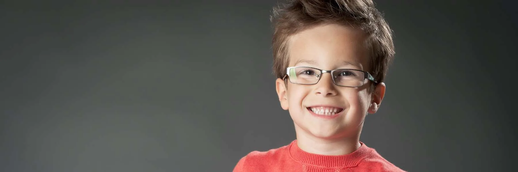 A boy wearing glasses against a dark background